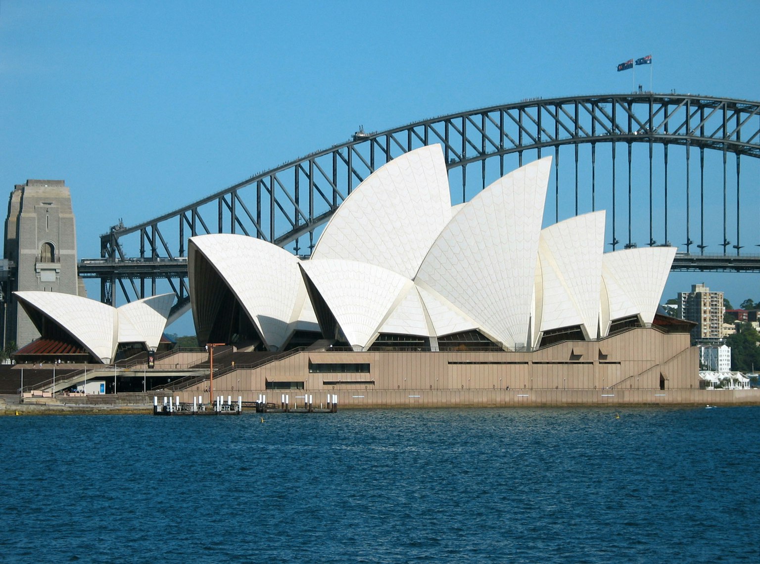 Sydney Opera House dengan atap putih berbentuk layar yang ikonik dan Jembatan Pelabuhan Sydney di latar belakang