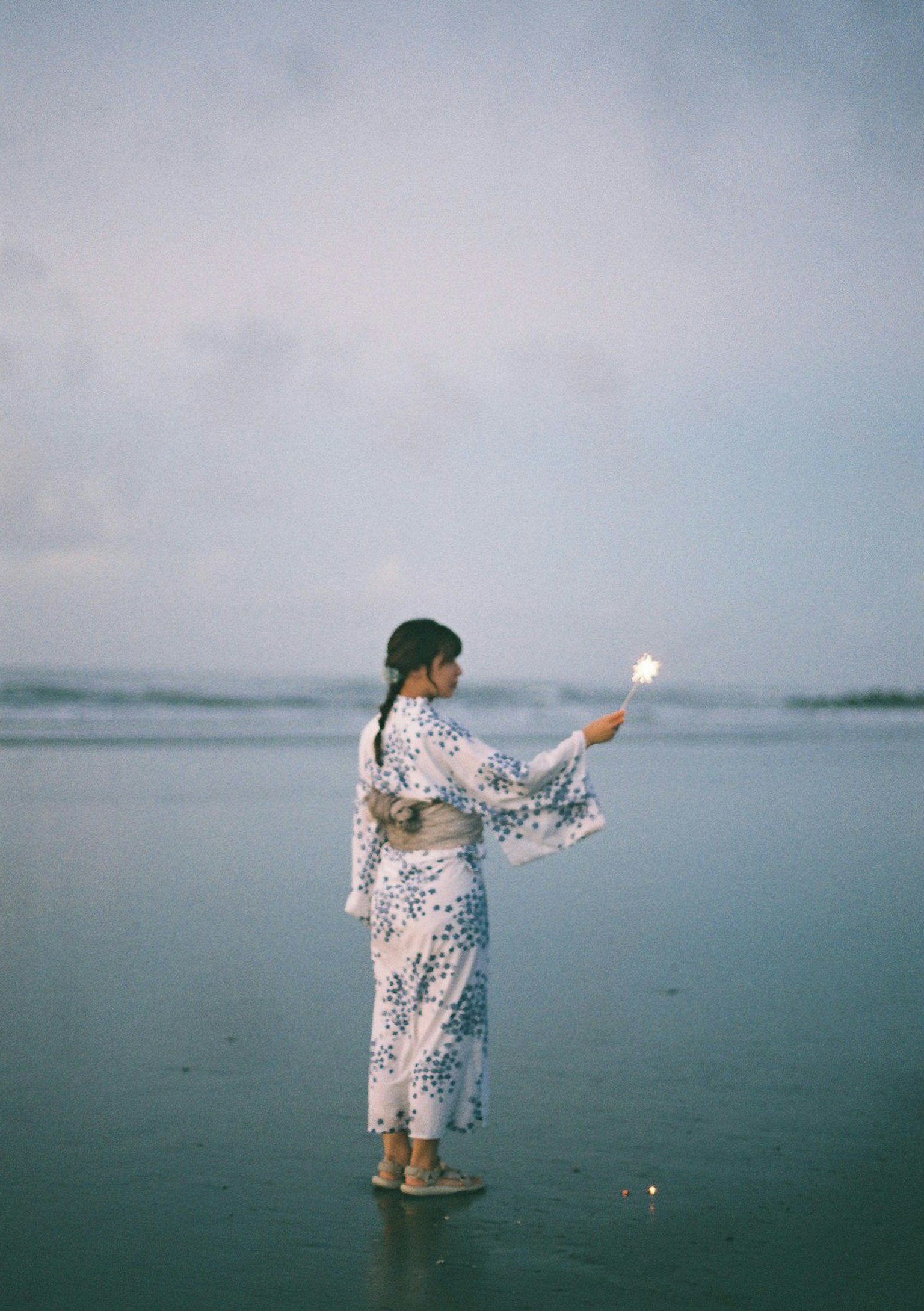 一位穿着和服的女性在海滩上站着拿着烟花