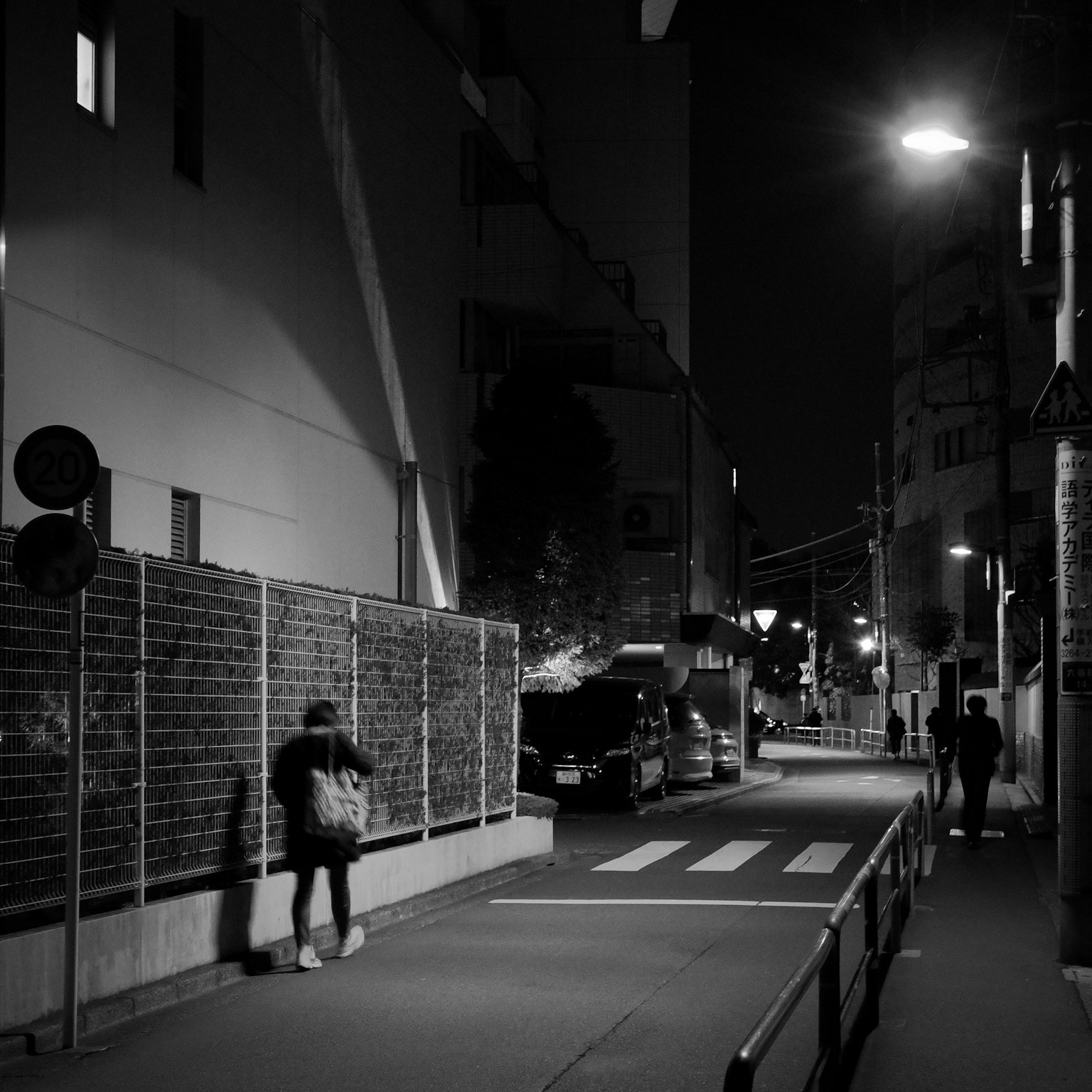 Una figura che cammina in una strada notturna con lampioni e ombre