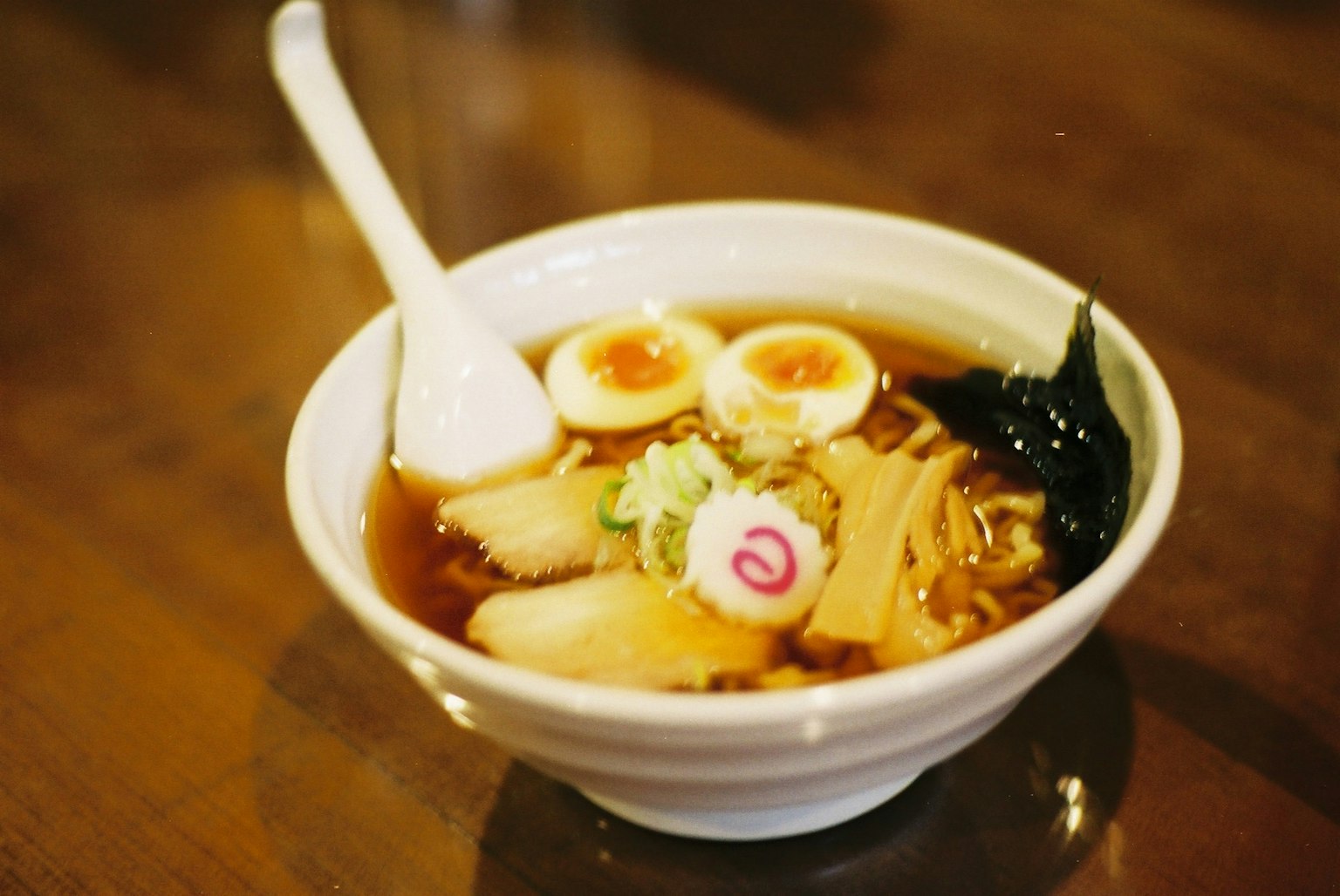 A bowl of ramen featuring chashu pork, soft boiled eggs, green onions, nori seaweed, and narutomaki