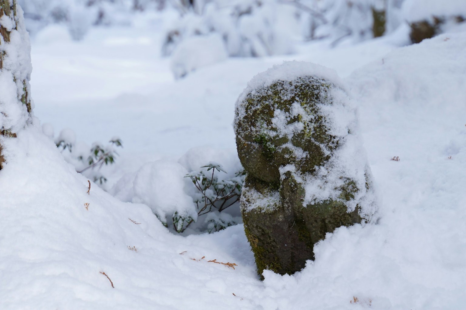 Une petite statue en pierre partiellement recouverte de neige près d'un paysage enneigé