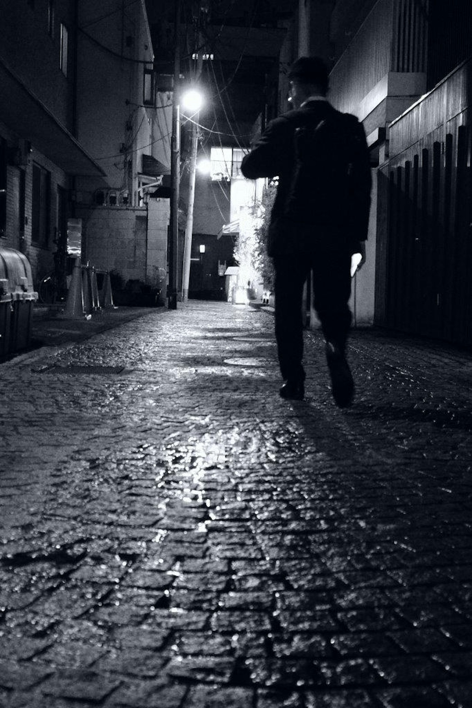 Silhouette di una persona che cammina in un vicolo notturno Sentiero in ciottoli e luce di un lampione