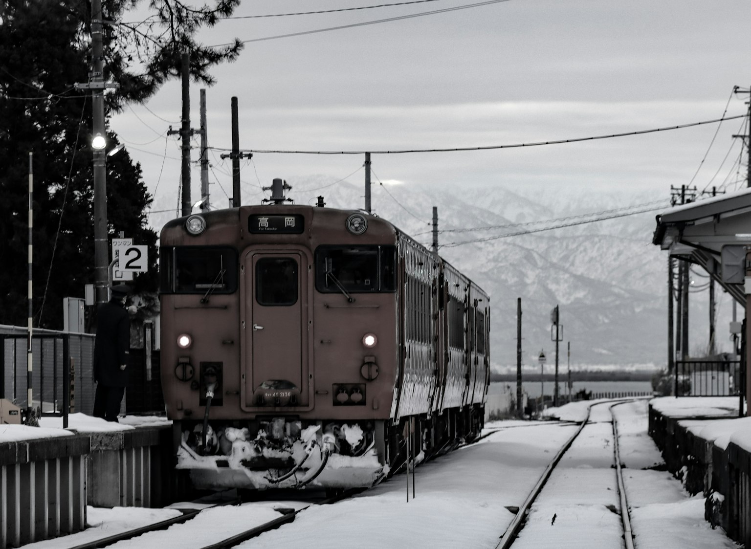 Treno fermo in una stazione innevata con montagne sullo sfondo