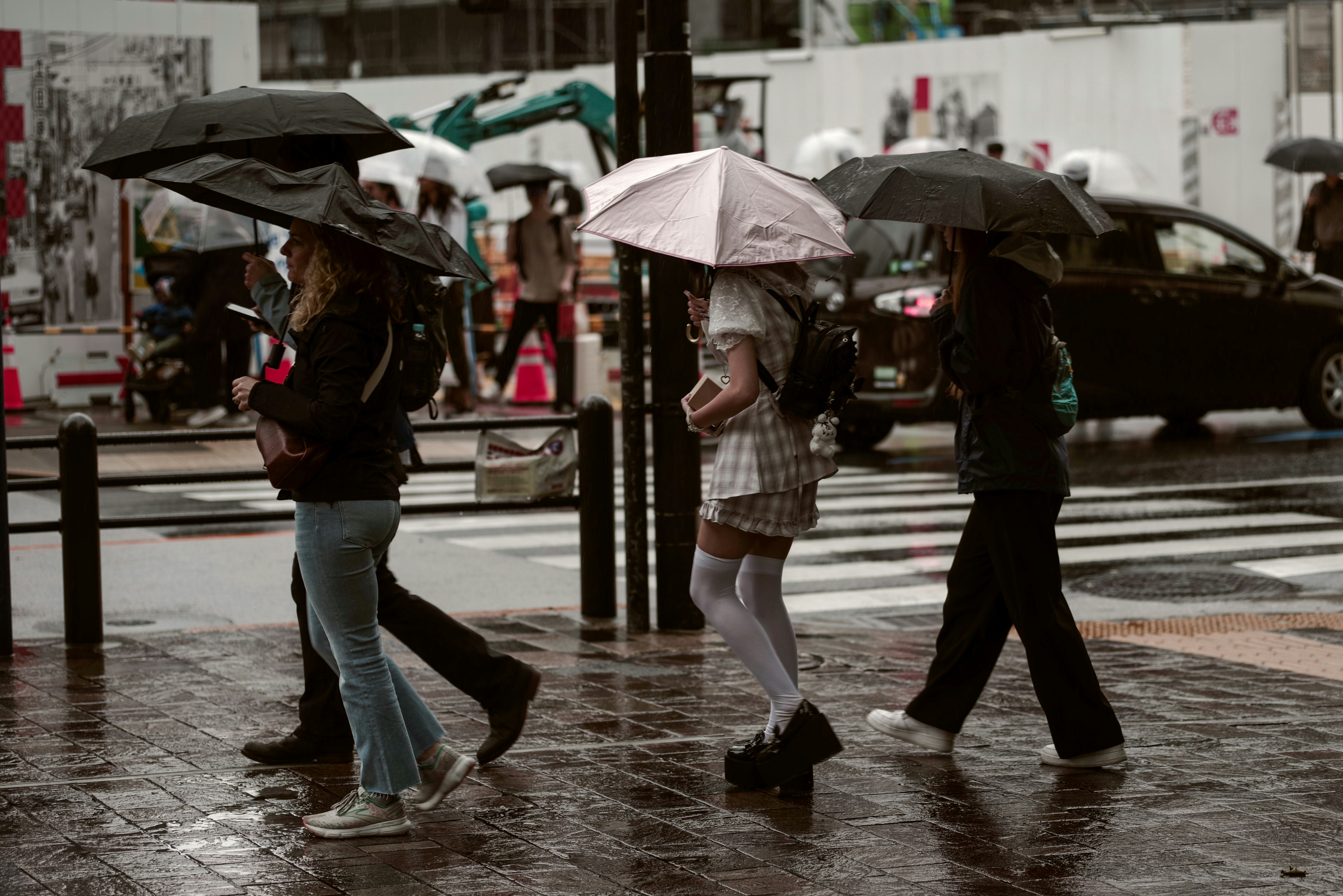 雨の東京の横断歩道を傘をさして歩く観光客の街並み