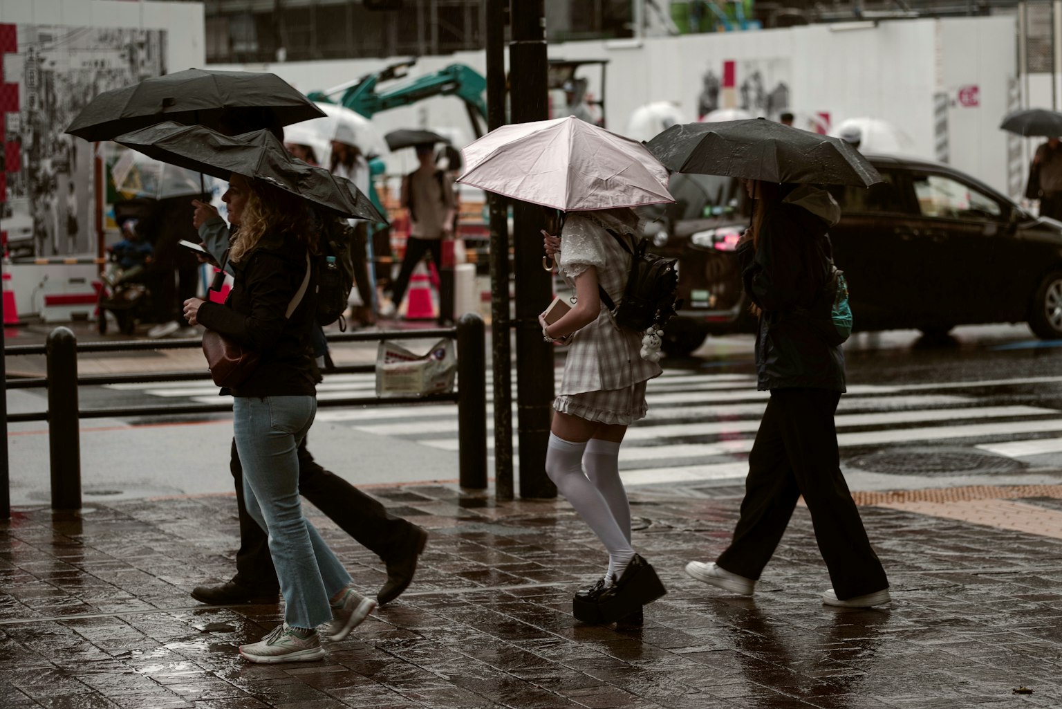 一群人在雨中撐著傘走過城市人行橫道的場景