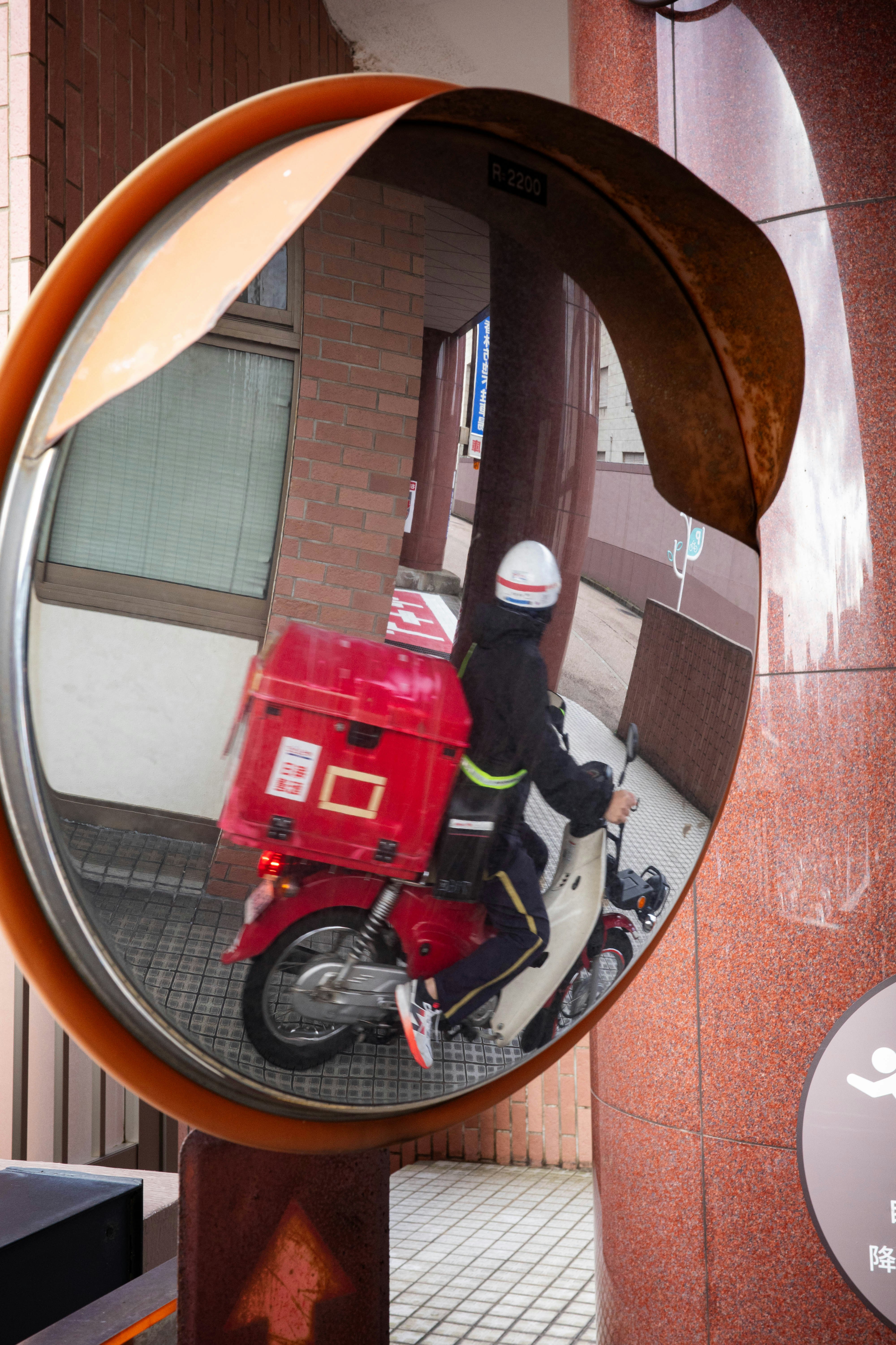 路地のアーチ型ミラー越しに赤いバイクと人が写る街角