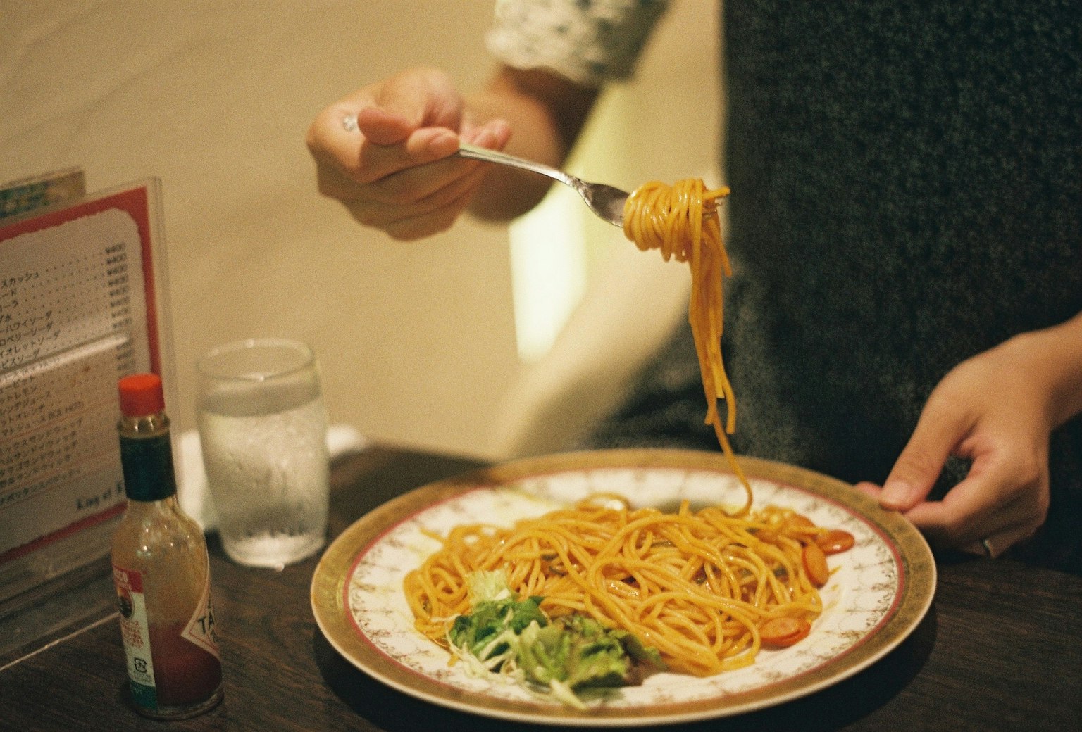 Mano che tiene una forchetta con spaghetti sopra un piatto di spaghetti
