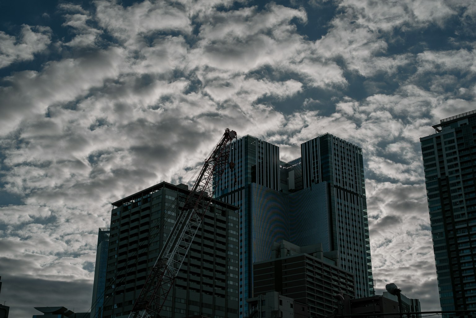 Silhouette bangunan tinggi dan crane di latar belakang langit mendung gelap