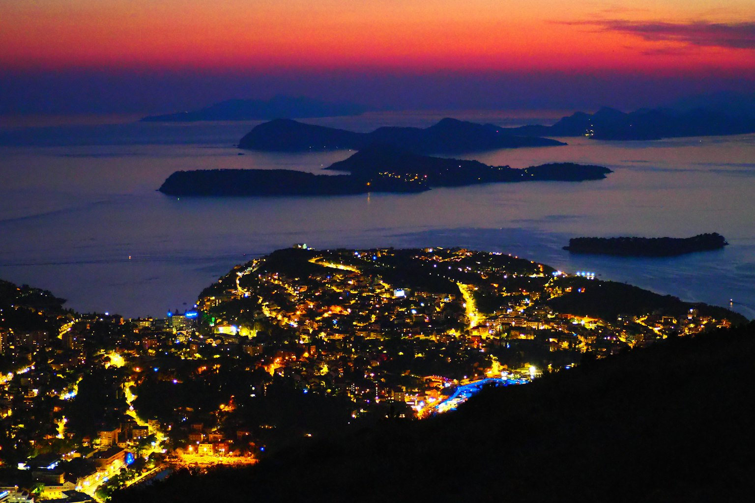 Stupenda vista notturna di una città costiera con luci brillanti e isole al tramonto