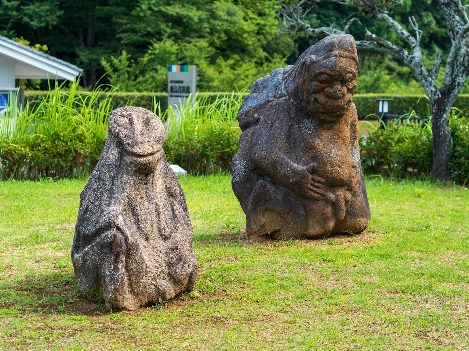 Zwei Steinstatuen in einem Garten eine ähnlich einer Frosch und die andere einer menschlichen Figur