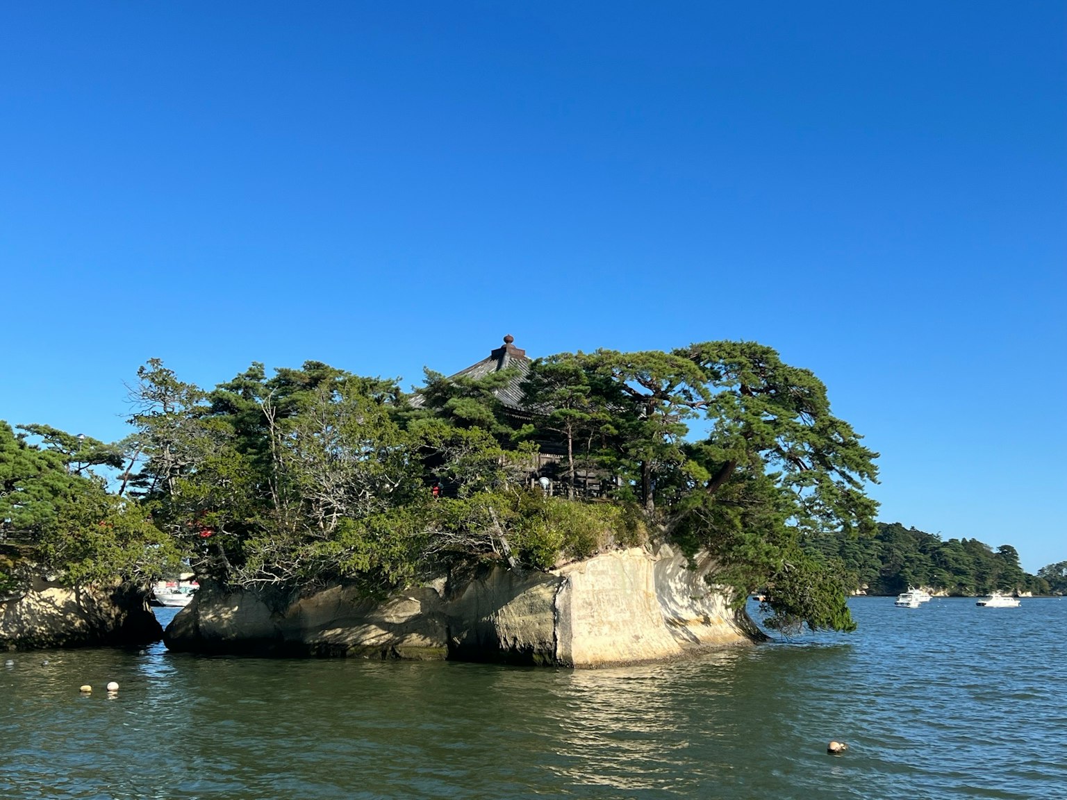 Una piccola isola con alberi rigogliosi sotto un cielo blu chiaro che si riflette su acque calme