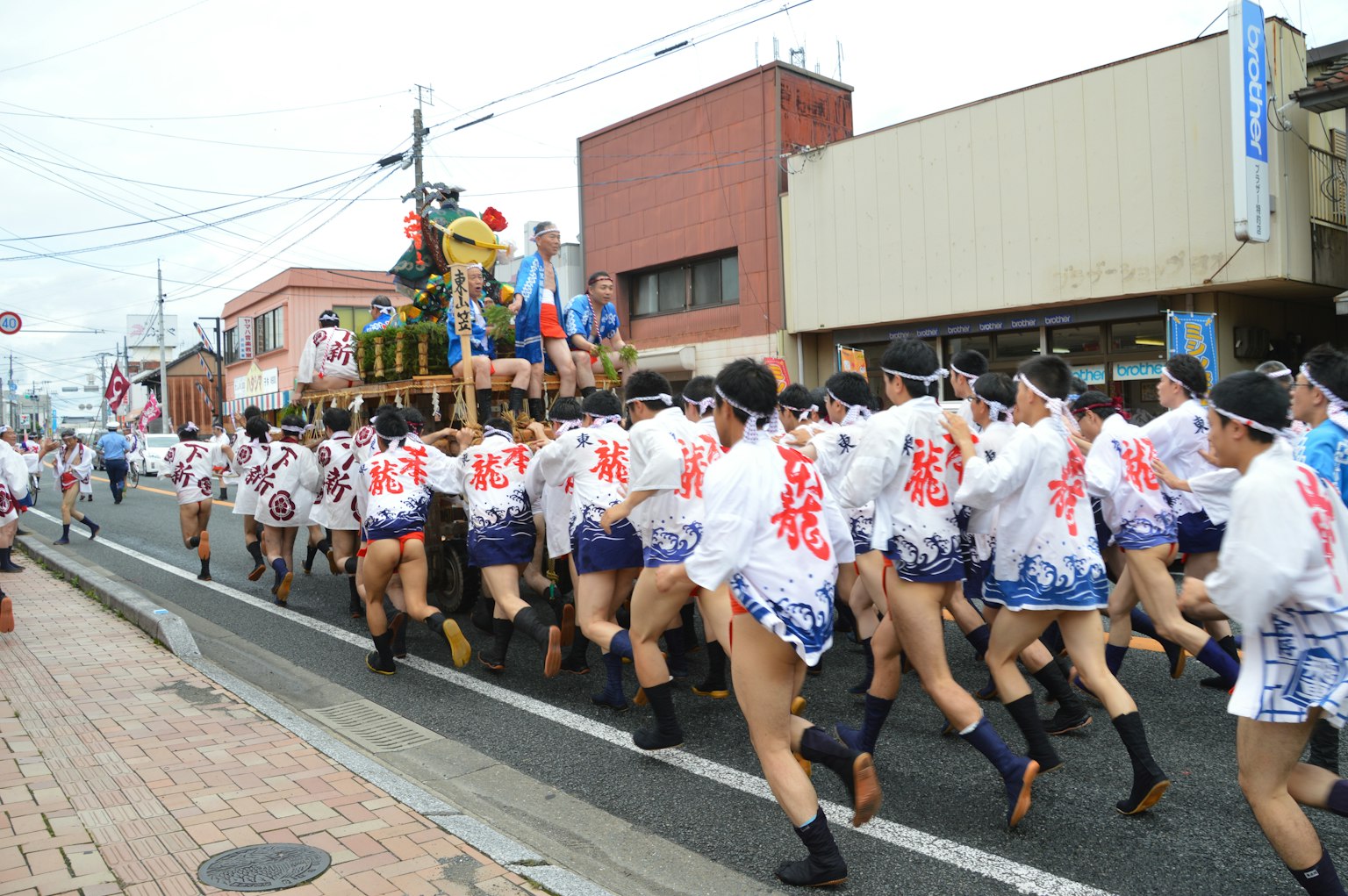 Line of men running in traditional festival attire with red patterns marching down a street