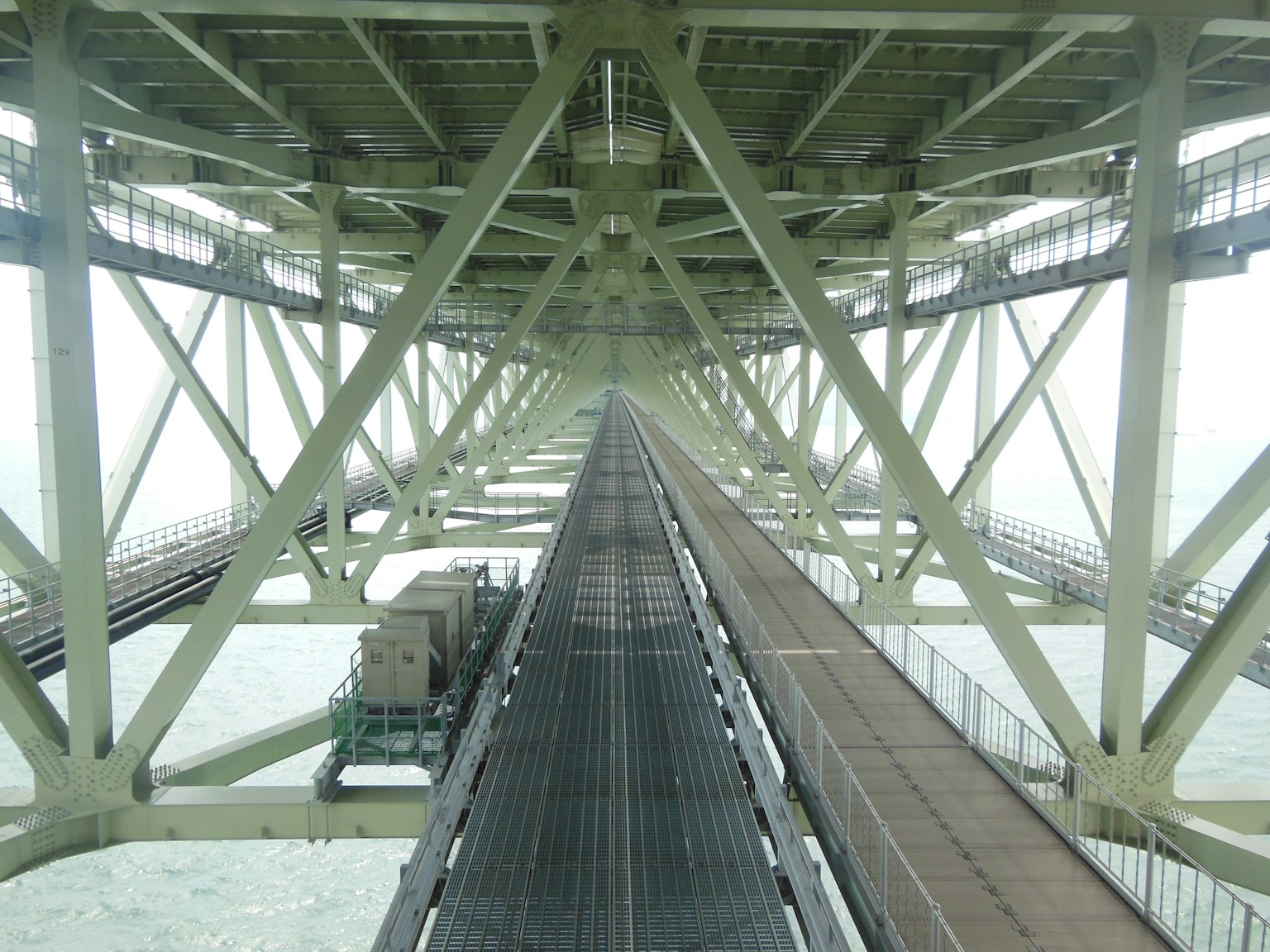 Blick von unter einem Brückenbauwerk mit strukturellen Elementen und Gleisen, die in die Ferne führen