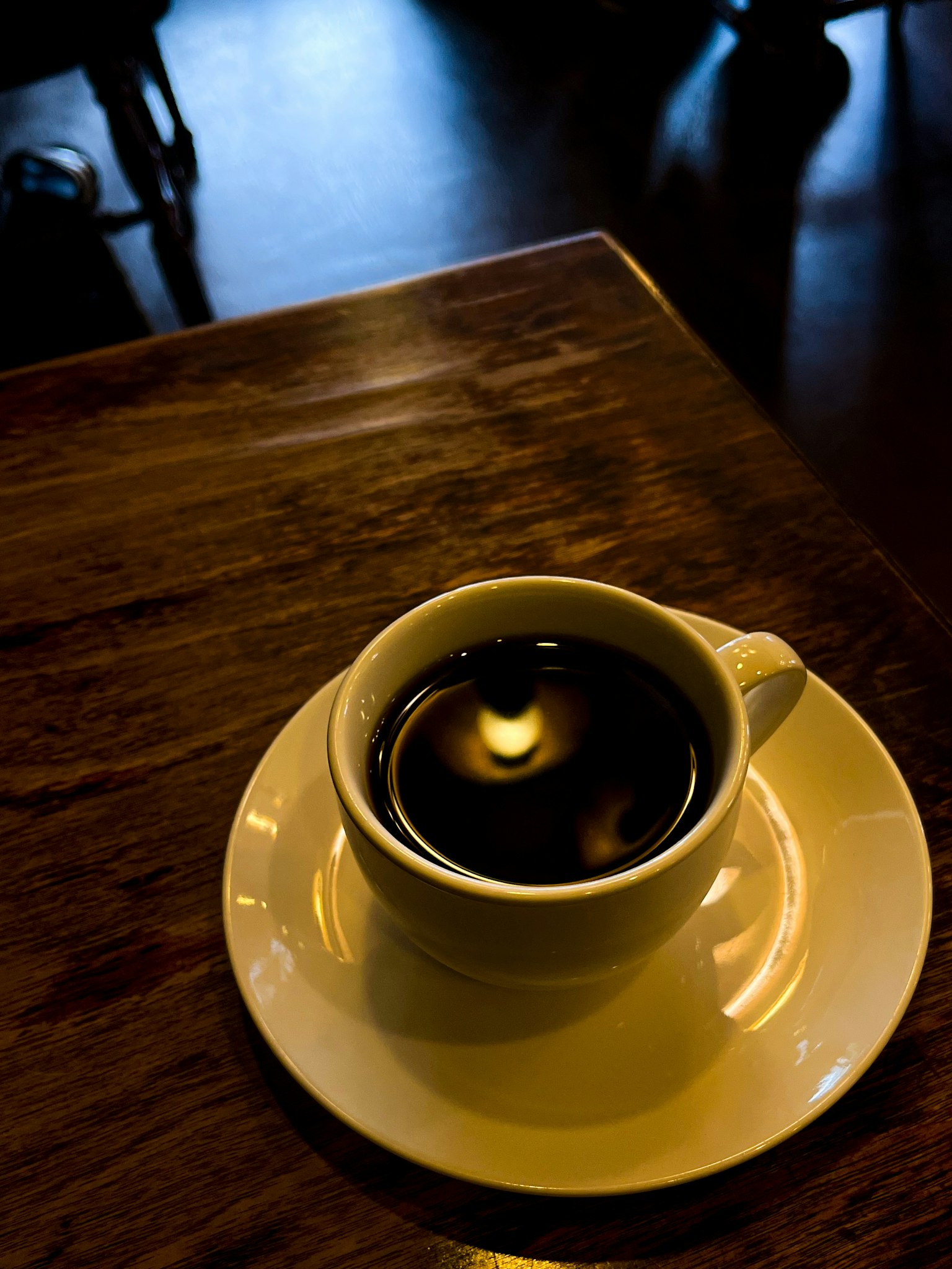 木桌上的白色咖啡杯，裡面裝著黑咖啡