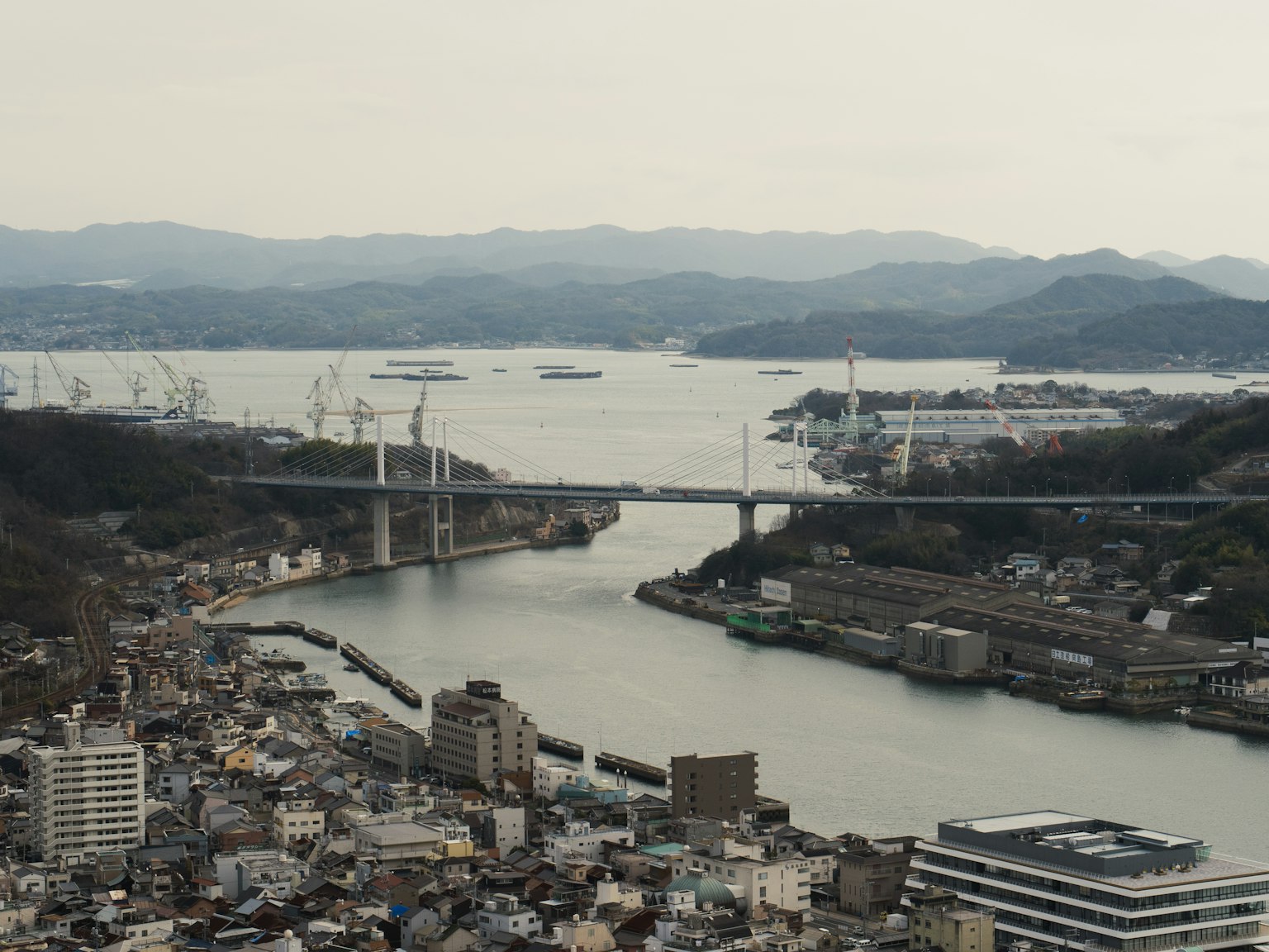 城市風景 背景為海和山 大橋橫跨河流 船隻停靠
