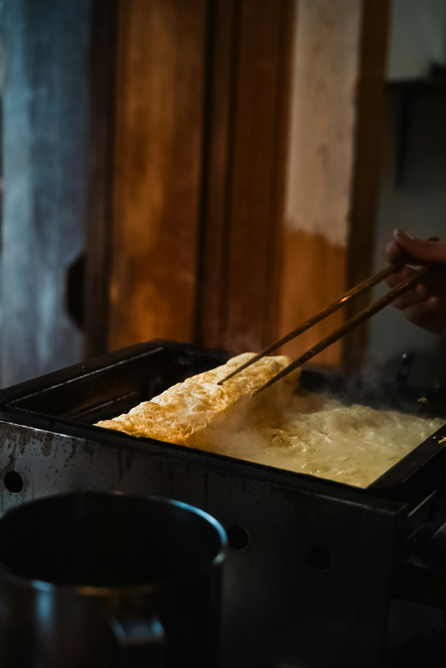 一隻手用筷子從油炸鍋中夾起食物