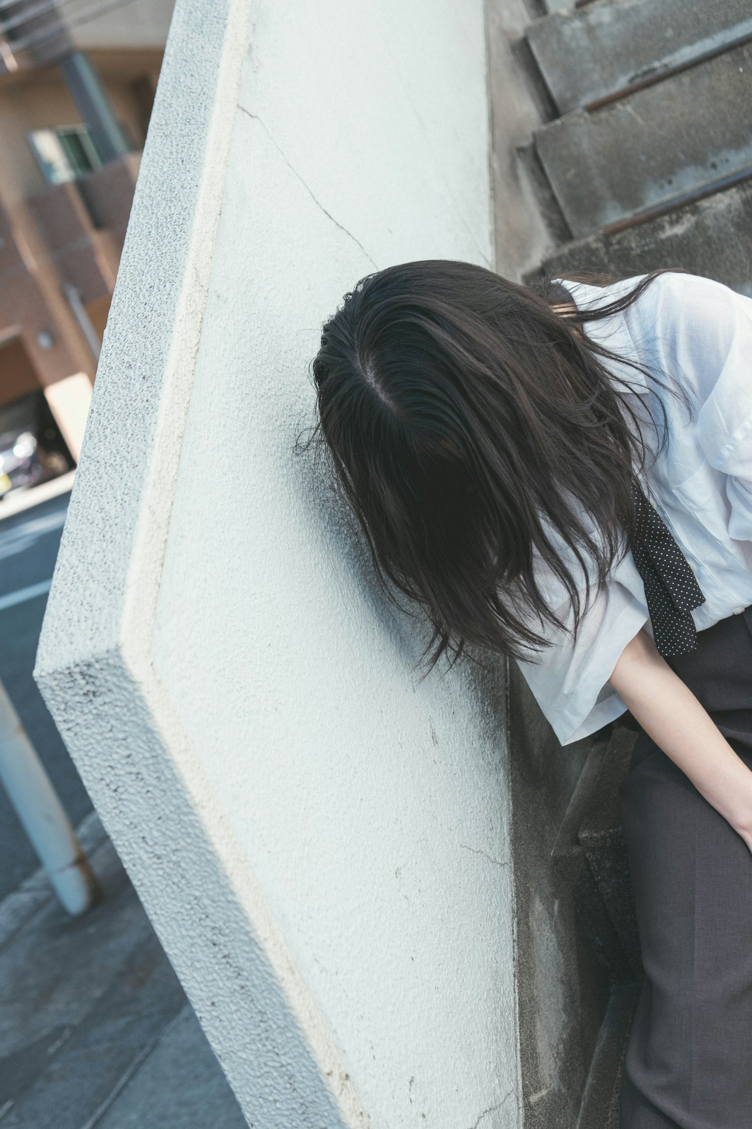 Una donna appoggiata a un muro con lunghi capelli scuri che indossa abiti casual