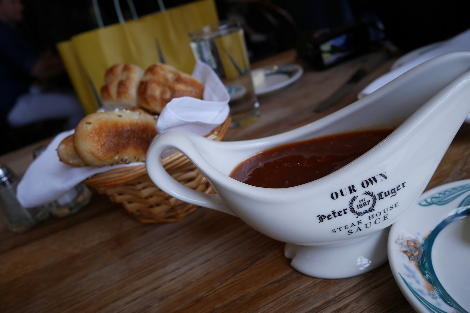 Nước sốt gravy trong thuyền trắng với giỏ bánh mì trên bàn ăn