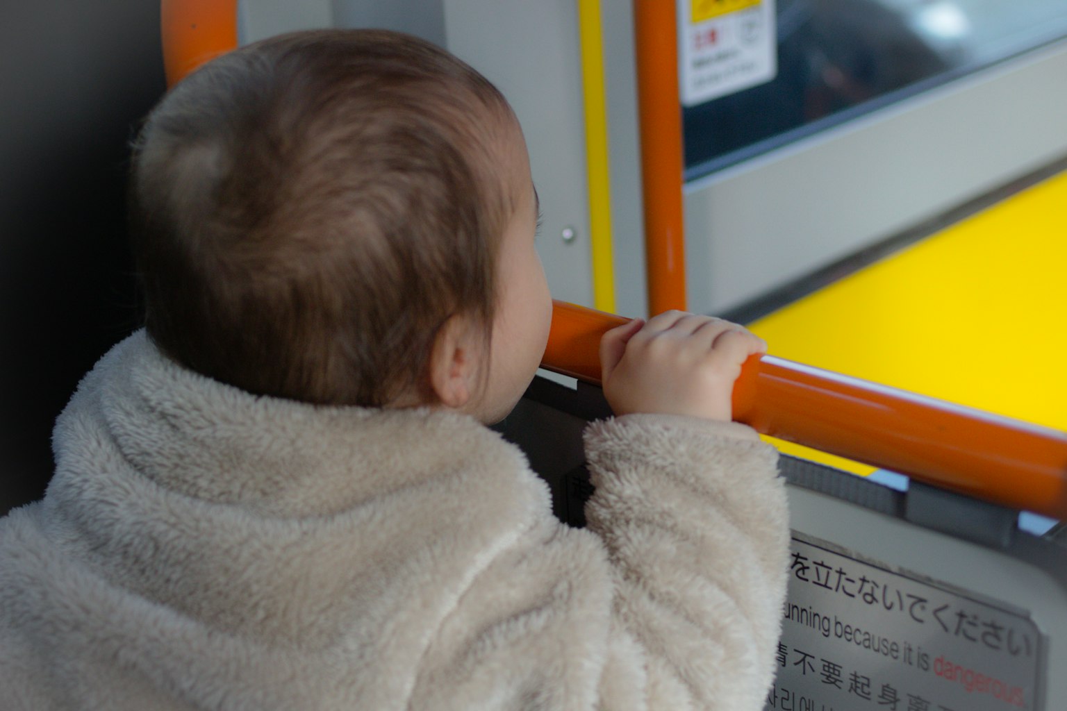 Un bebé apoyado en una barandilla naranja mirando por la ventana
