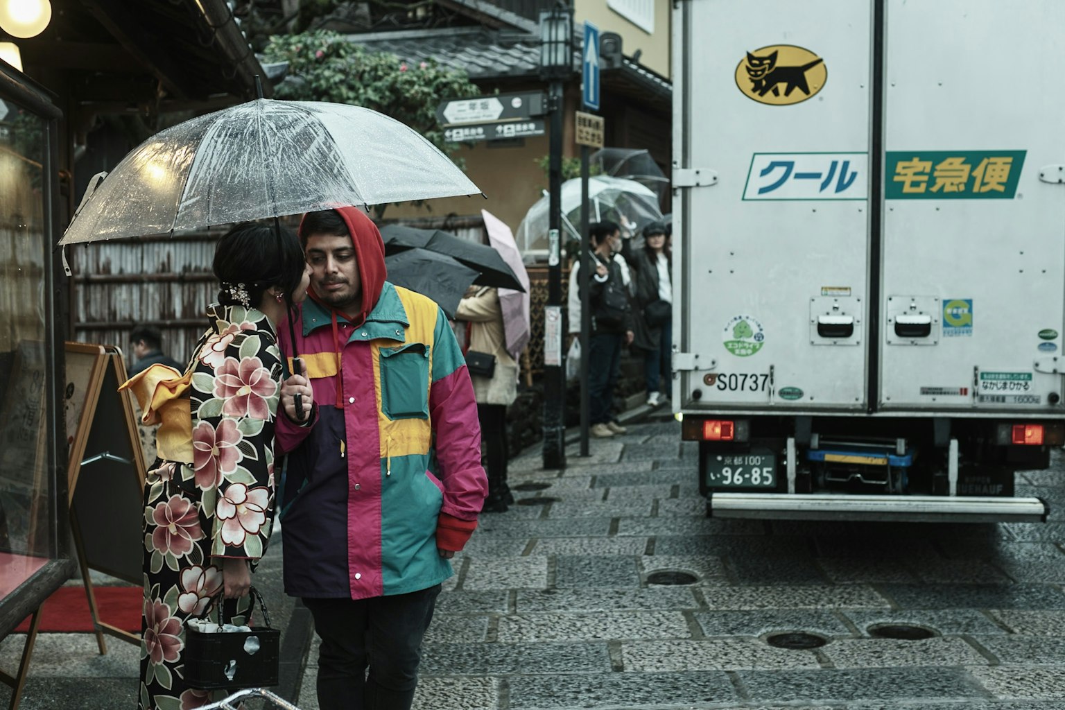 兩個人穿著色彩繽紛的衣服，在雨中撐著傘走在城市街道上