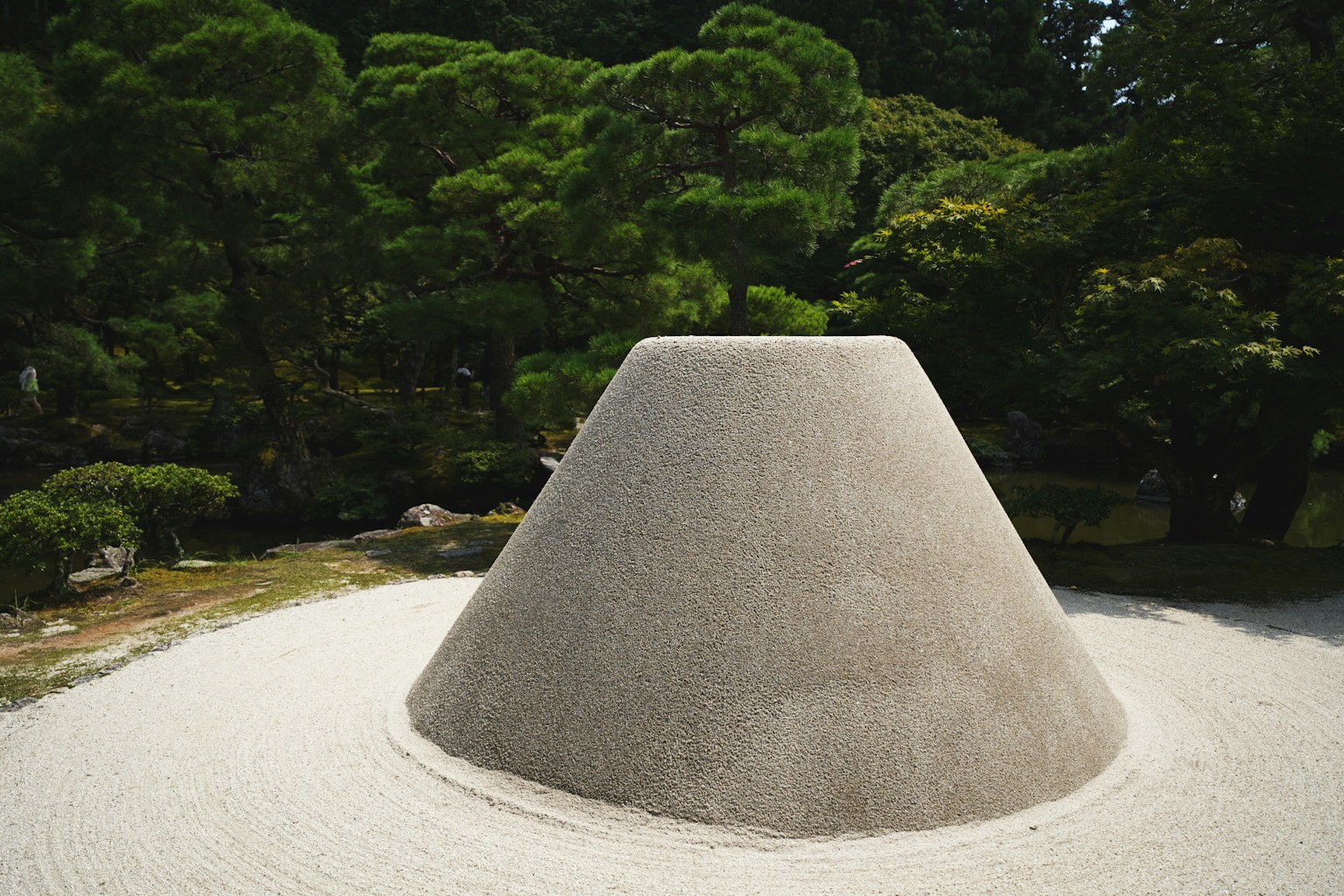 Struktur batu berbentuk kerucut di taman dikelilingi oleh tanaman hijau
