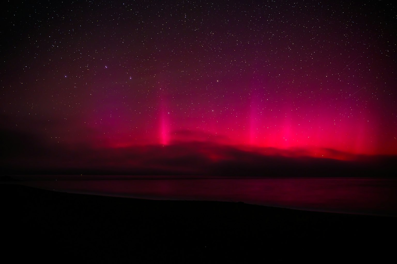 Vibrante rosa Aurora über einem dunklen Ozean unter einem sternenklaren Himmel