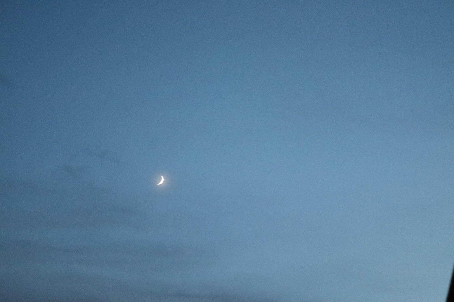 Luna creciente en un cielo azul con nubes delgadas