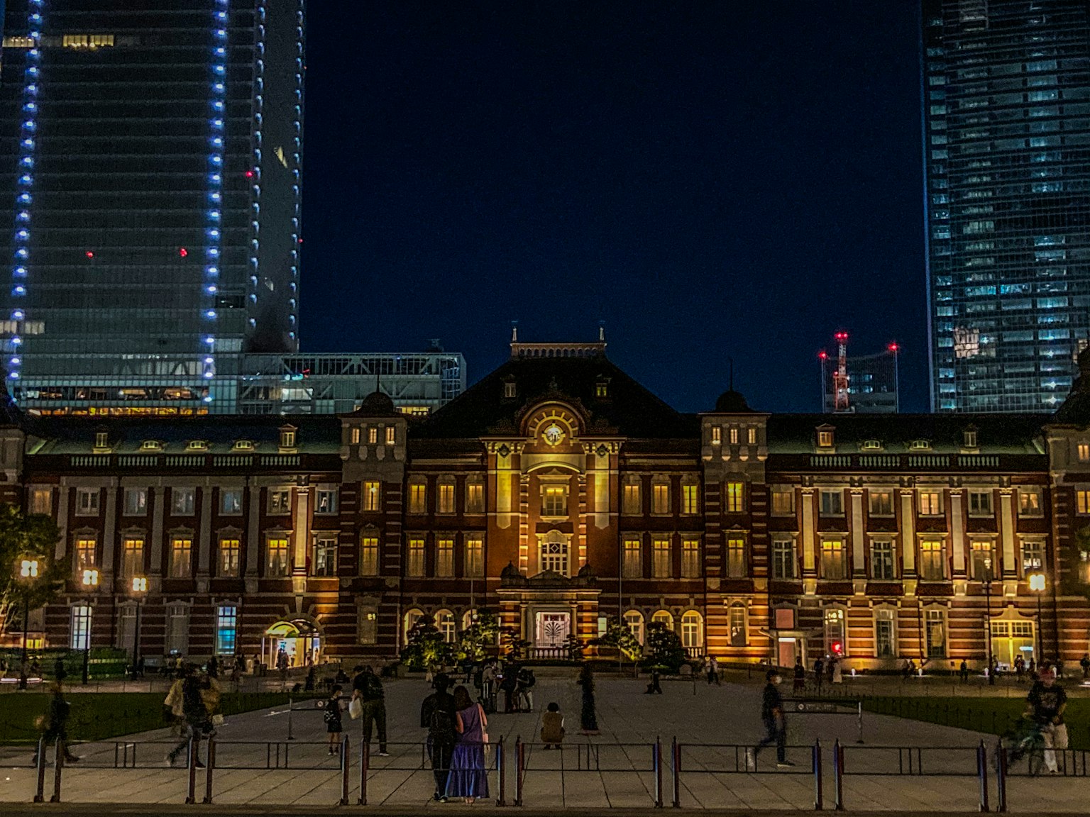 Stasiun Tokyo di malam hari dengan pencahayaan cerah dan gedung pencakar langit modern di sekitarnya
