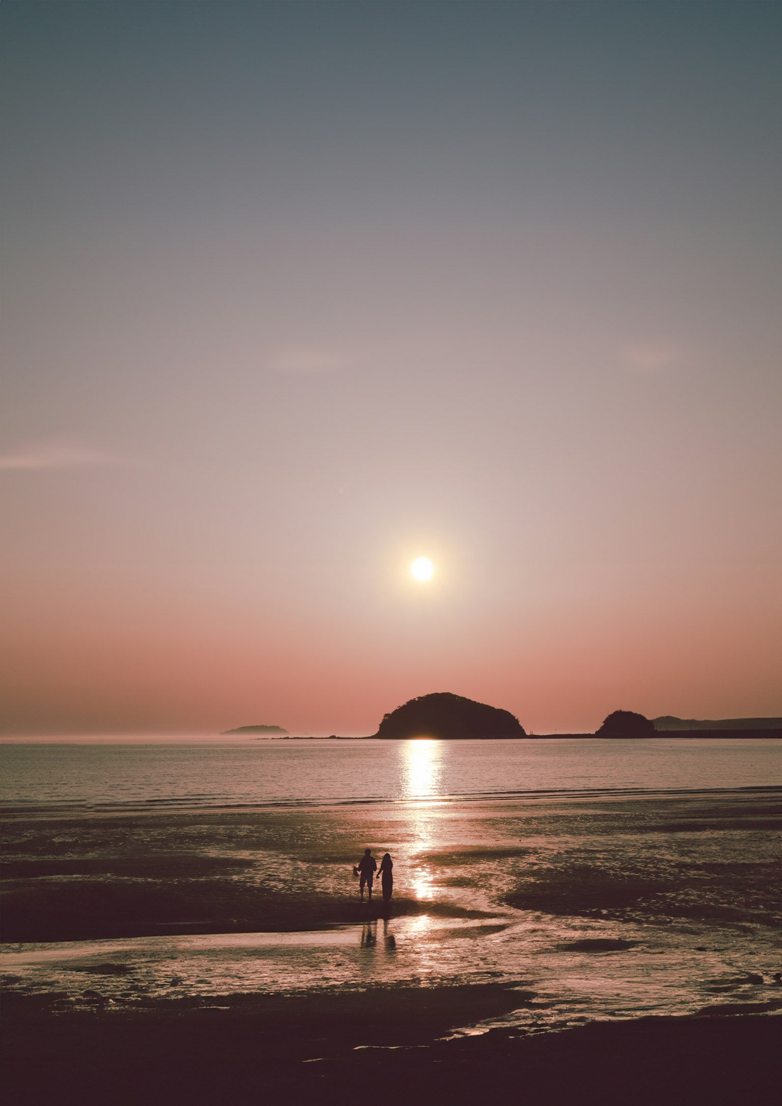 夕日を背景に海岸で立つカップルと静かな海の風景