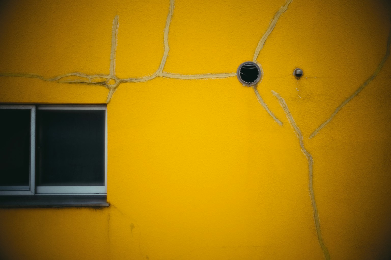 Mur jaune avec des fissures et un objet rond noir