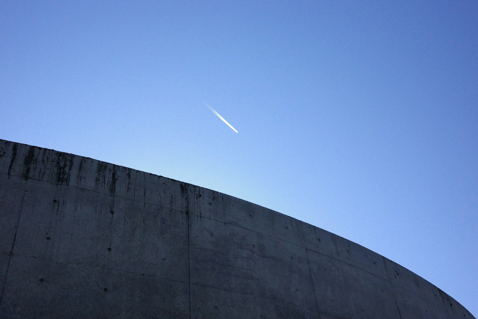 Trace de condensation blanche dans le ciel bleu au-dessus d'une structure en béton courbe