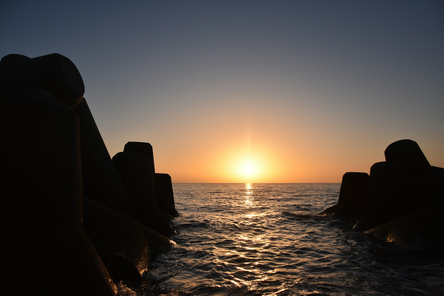 Silhouette of breakwaters against a sunset over the ocean