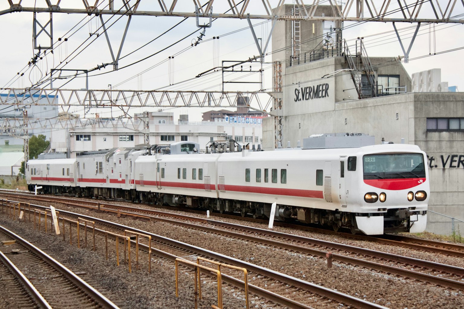 一列白色火車在軌道上行駛，背景是建築和高架線