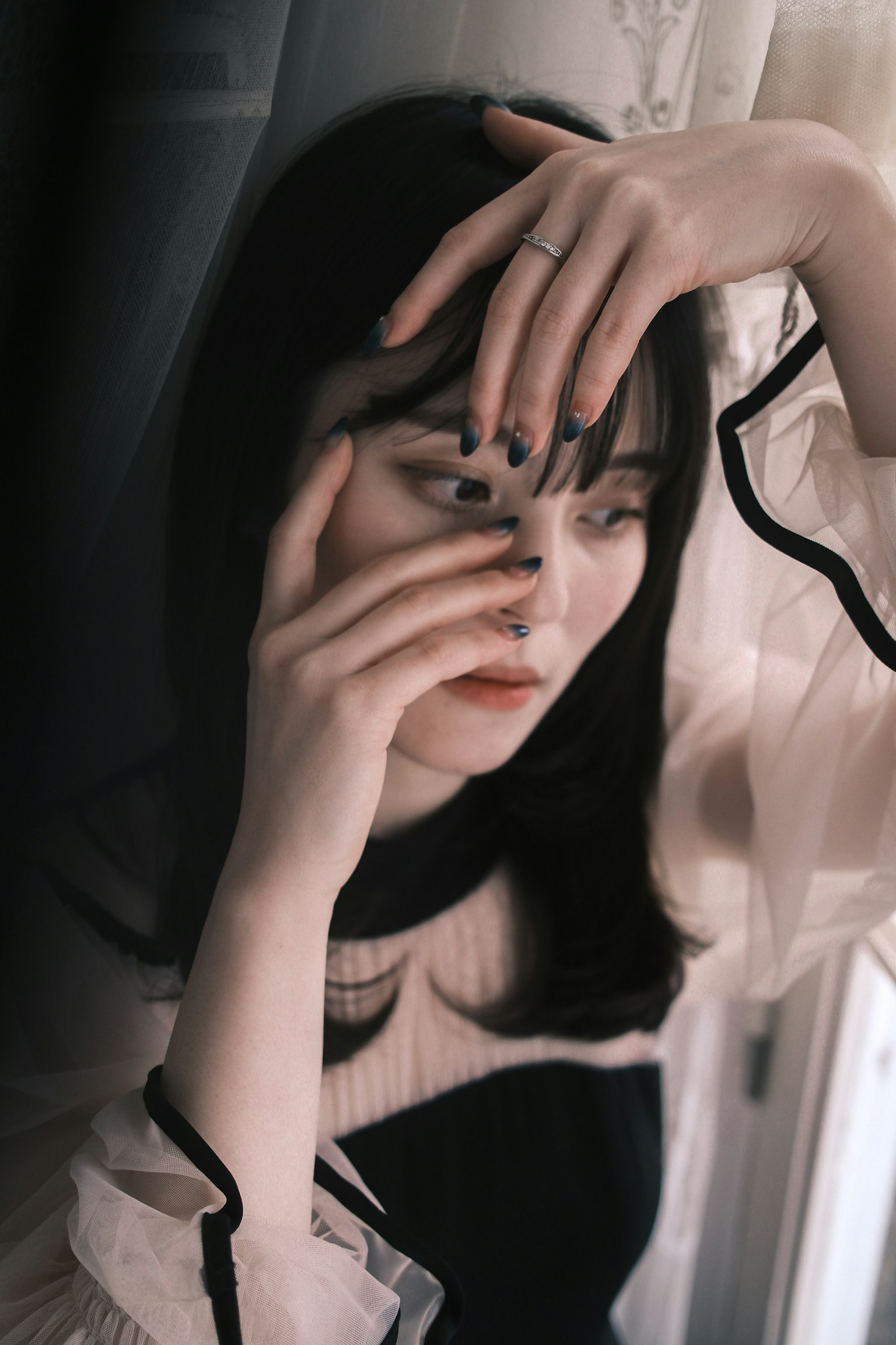 窓辺でポーズをとる女性の肖像写真 手で顔を隠すようにしている 黒と白の服を着ている
