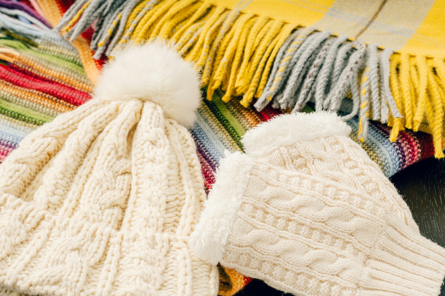 Weißer Strickhut und Handschuhe auf einer bunten Decke