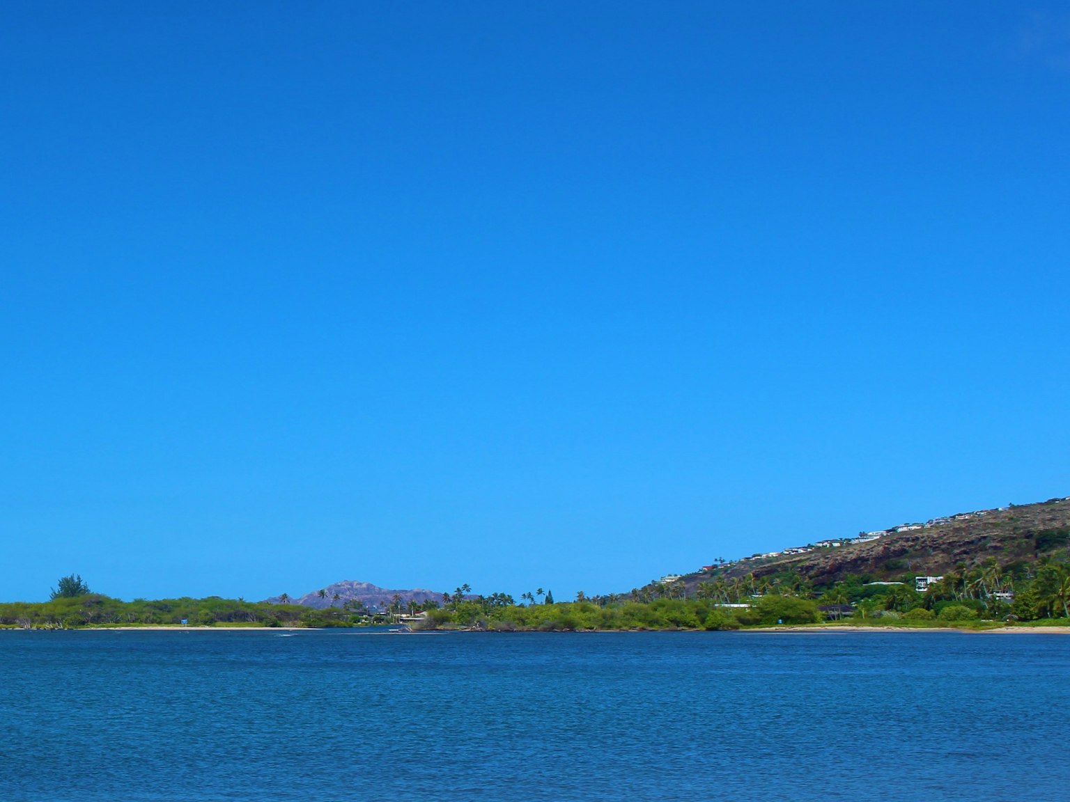 Paisaje con cielo azul claro y superficie de agua tranquila con colinas verdes a lo lejos