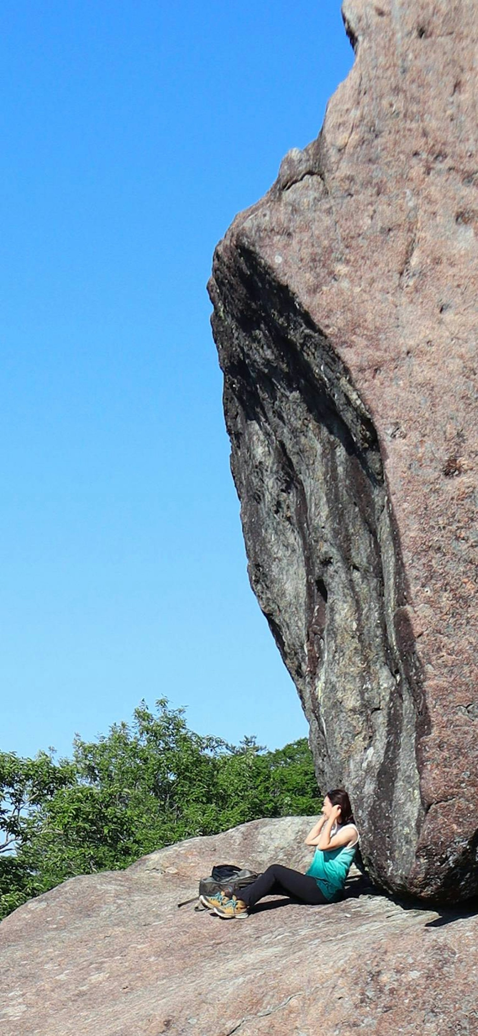 Woman sitting in the shade of a large rock under a clear blue sky