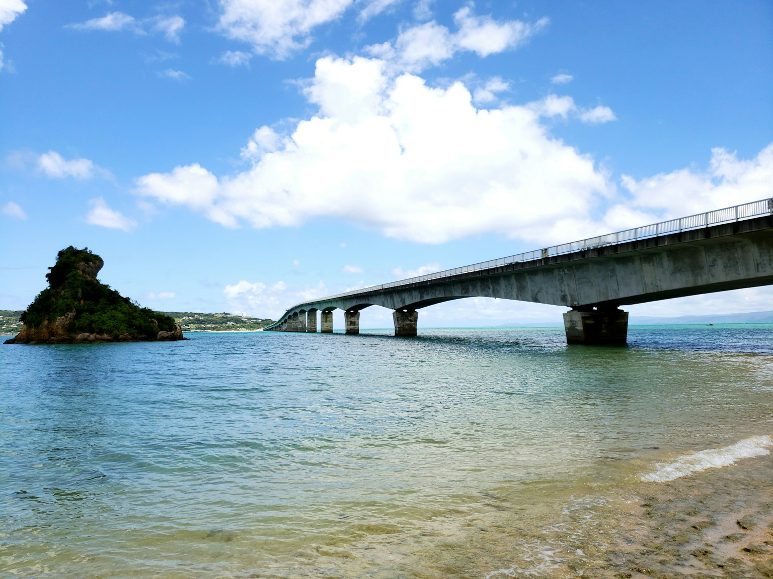 Puente sobre agua clara con una roca isleña bajo un cielo azul