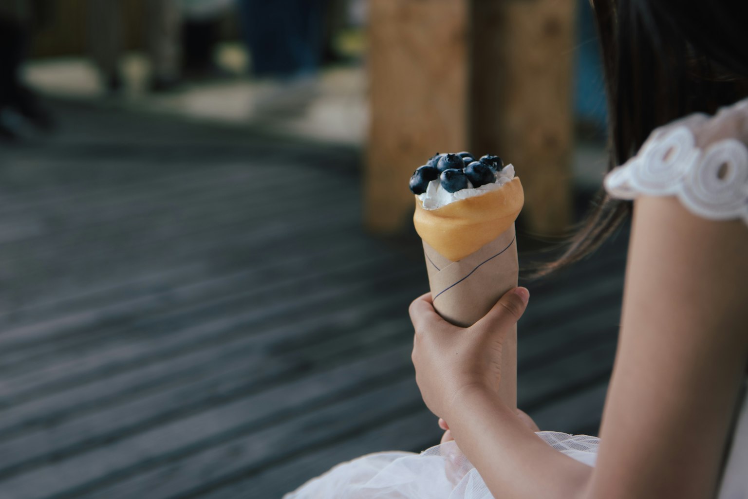 Eine Hand, die einen Eisbecher mit gelber Spitze und Blaubeeren hält