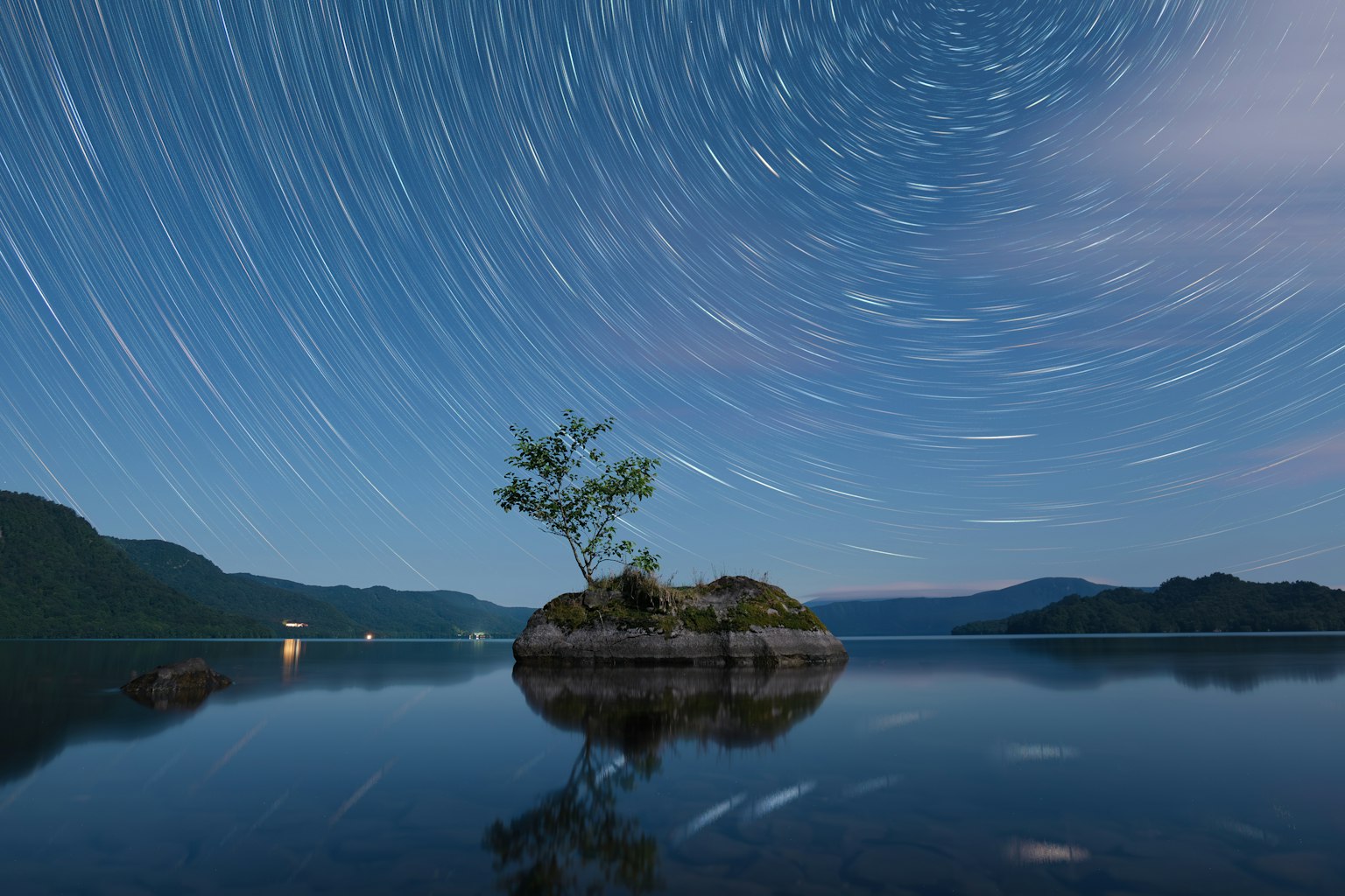 Eine kleine Insel mit einem Baum unter einem Sternenhimmel, der Sternspuren zeigt
