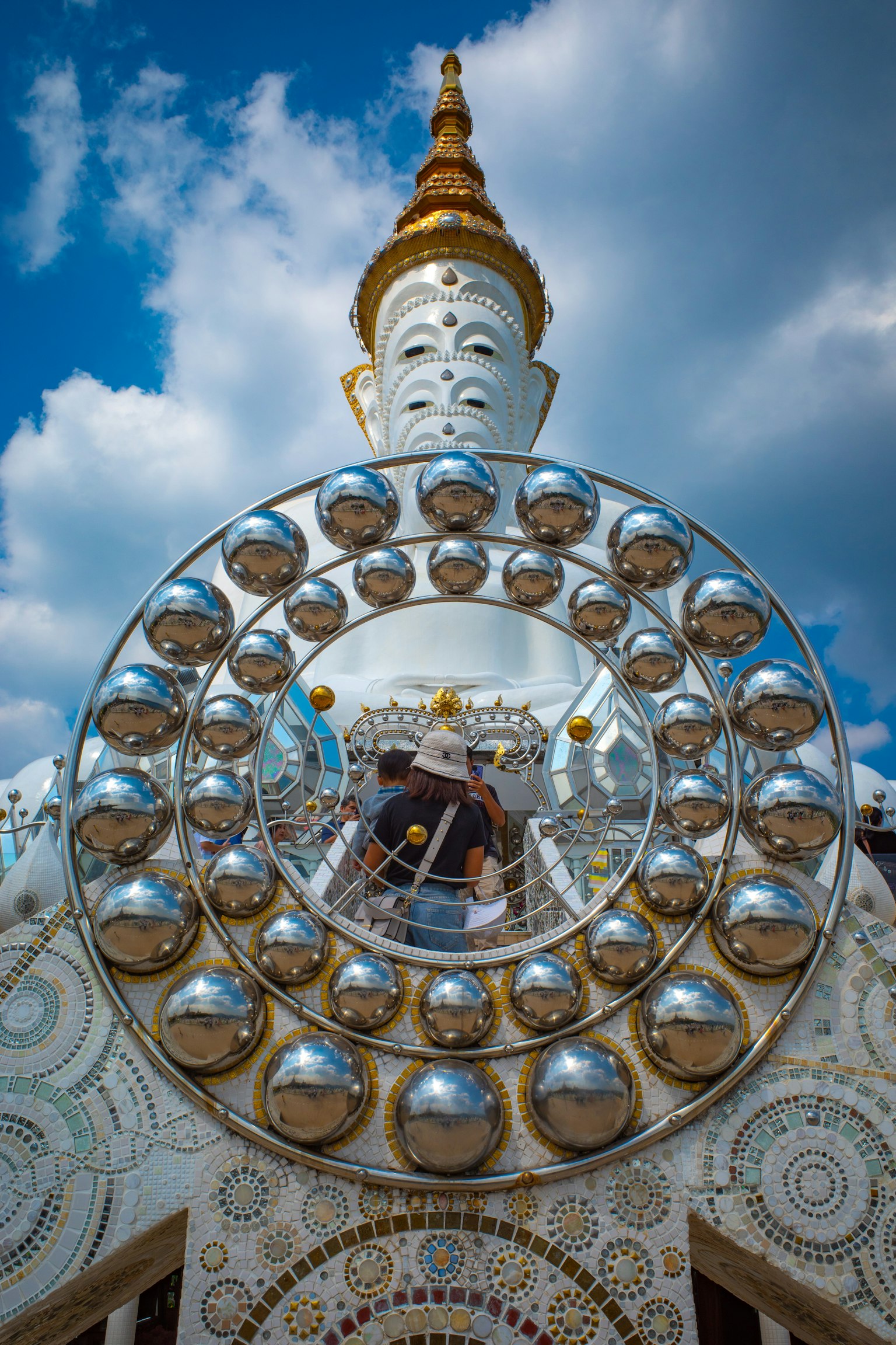 Tampilan luar sebuah kuil dengan patung Buddha putih dan menara emas Dekorasi berbentuk lingkaran seperti cermin menciptakan desain yang mengesankan