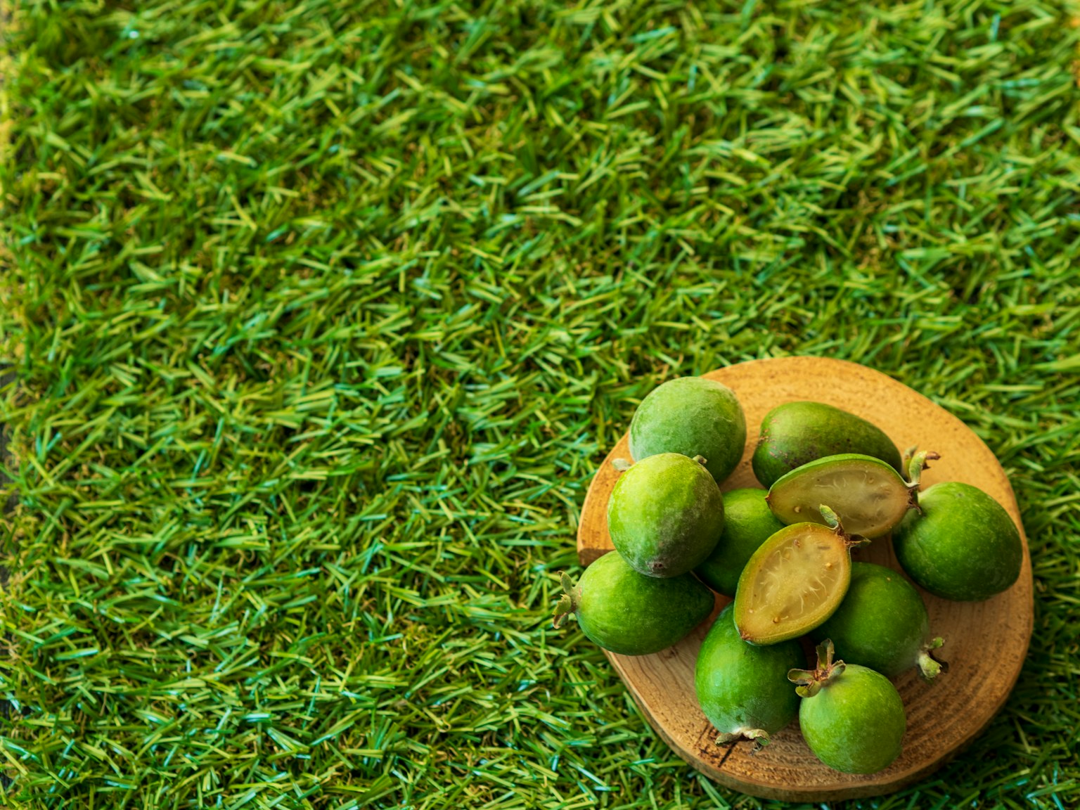 A wooden bowl filled with unripe green fruits placed on green grass