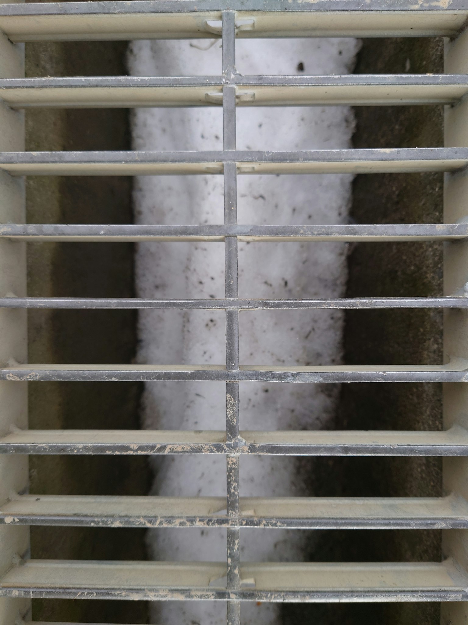 Grill ventilasi logam dengan slat horizontal yang menunjukkan permukaan putih di belakang