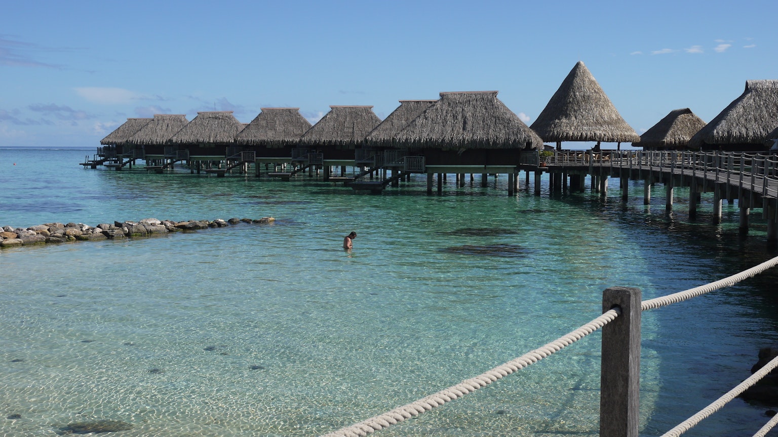 Bungalows sur pilotis sur une mer bleu clair avec une personne nageant