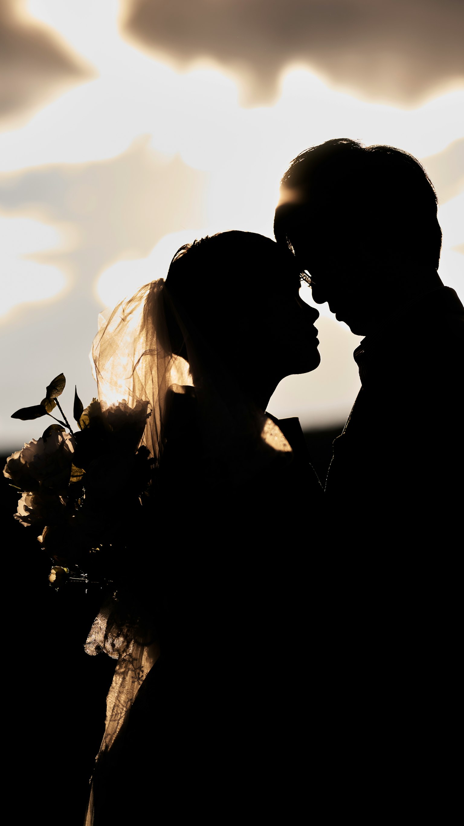 Silhouette d'un couple de mariés s'embrassant contre un fond de coucher de soleil