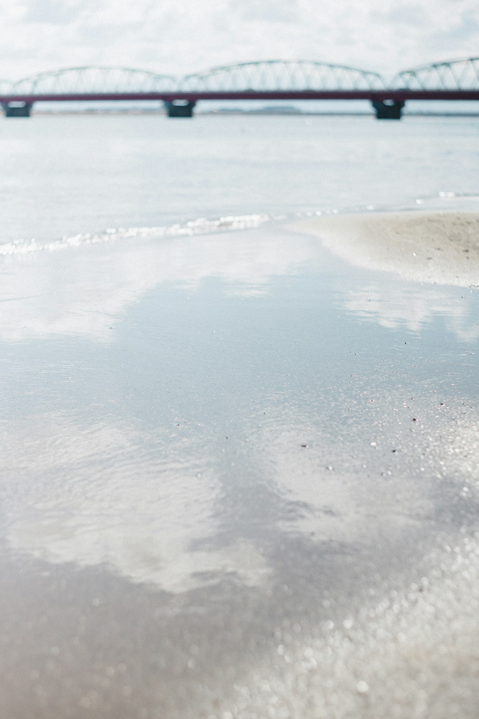 Superficie d'acqua calma che riflette un ponte e nuvole