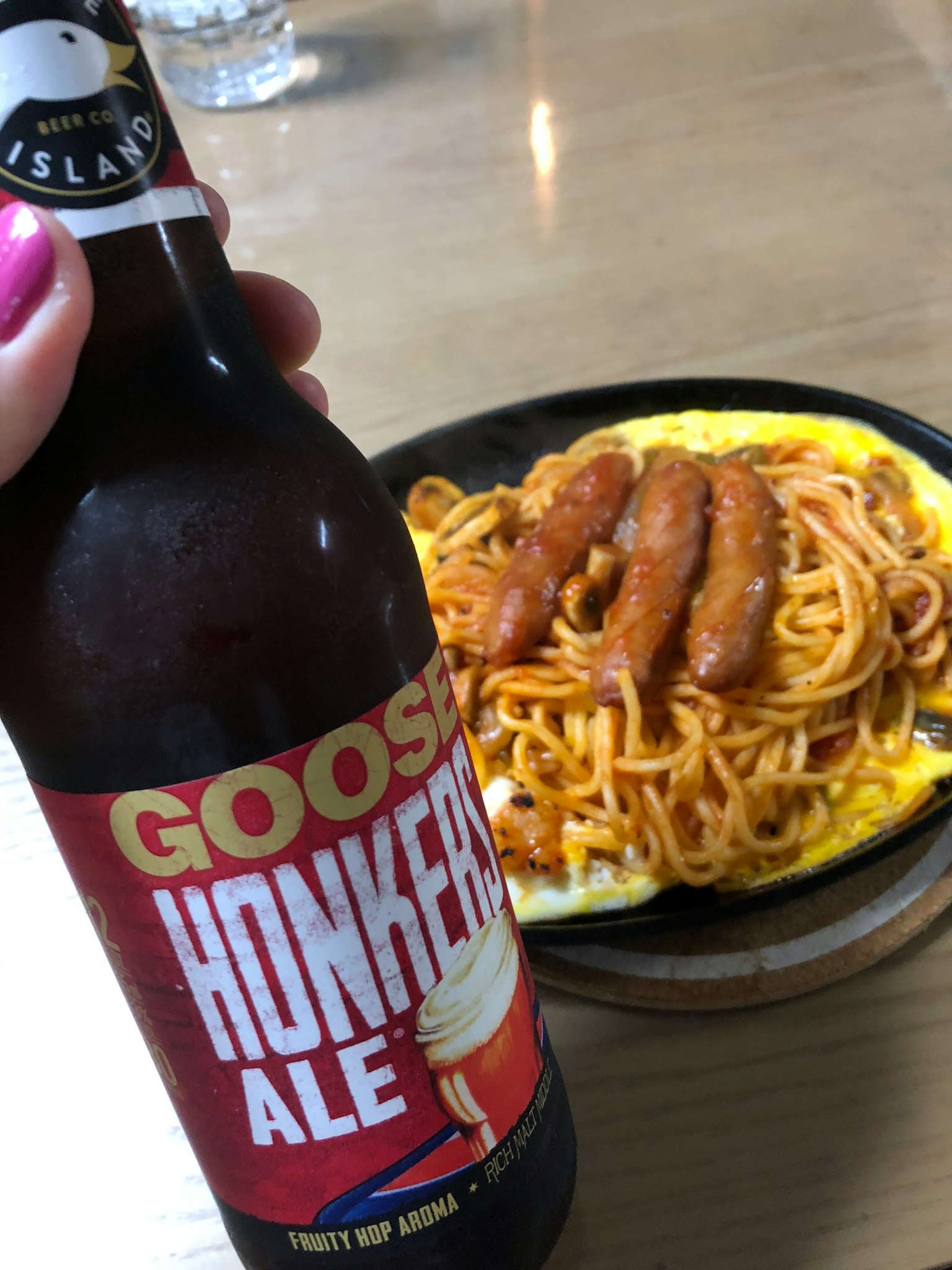 Goose Honker's Ale in hand with spaghetti and sausage on a plate