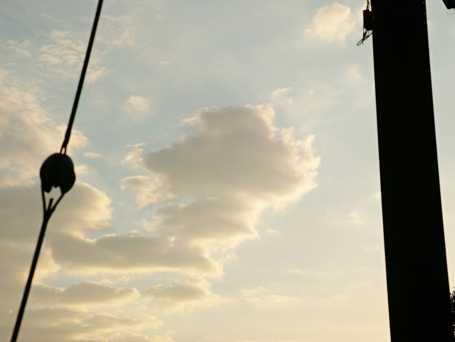 Silhouette eines Strommasts vor einem Sonnenuntergangshimmel mit Wolken