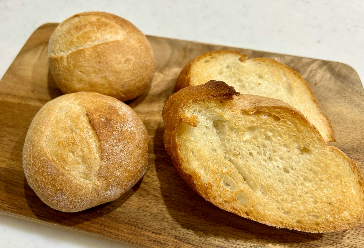 Tre panini e una fetta di pane su un tagliere di legno