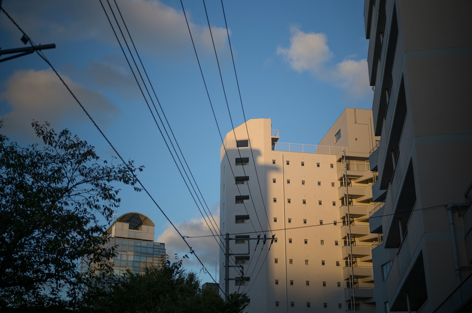 Cityscape featuring buildings and power lines under a blue sky with clouds